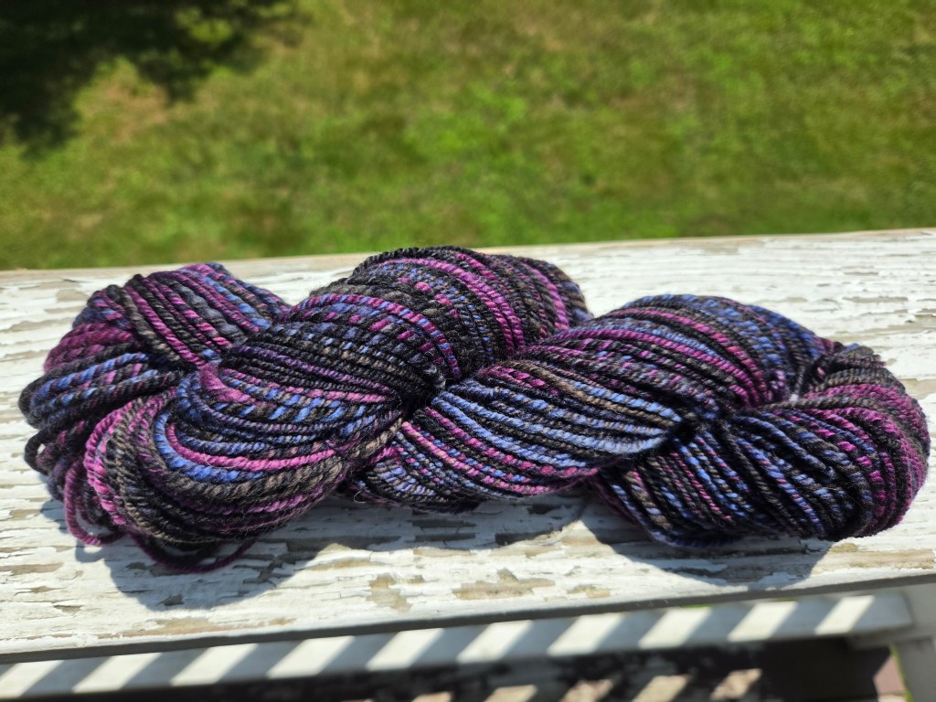 a skein of yarn in bright sunlight, in shades of black, pink, purple, and light blue